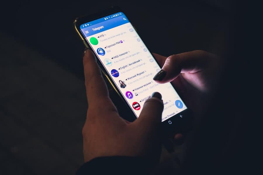 Fotografia raffigurante uno smartphone tenuto in mano. Lo schermo mostra l'applicazione Telegram con visibili alcune chat in lingua russa.